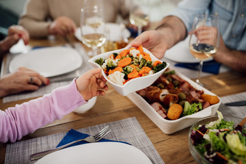 Close-up of parent and child passing food during lunch at dining table.