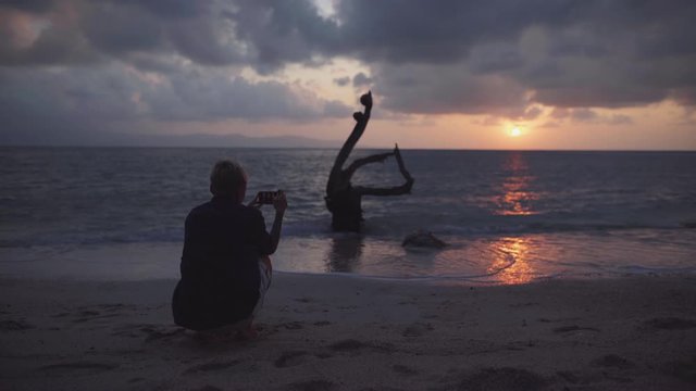 silhouette of a human taking a picture of sunset on a tropical beach