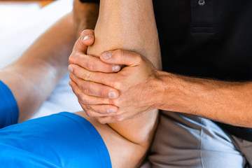 An unrecognizable professional sports masseur working on legs of sportsman after injury. Osteopathy and sports injury rehabilitation concepts - obrazy, fototapety, plakaty