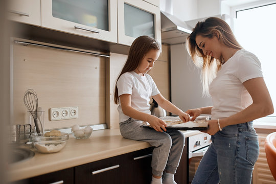 Beautiful Blonde Mother And Daughter Baking Cookies Together, Holding Tray Of Raw Cookie Dough, Hobby, Lifestyle, Free Time, Spare Time. Close Up Side View Photo