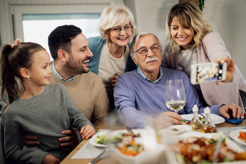 Happy extended family using smart phone and taking selfie in dining room.