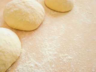 three balls of pizza dough on a rustic wooden background with flour dust