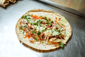 Open shawarma with chicken meat vegetables, cabbage, herbs and white pita sauce on a metal surface. Tasty street food kebab