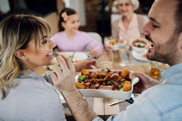 Happy man feeding his wife while having lunch with their family.