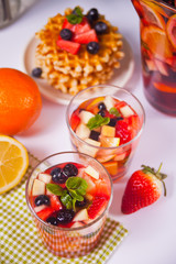 Red wine fresh sangria or punch with fruits, mint leaves and berries. Homemade waffles on the background.