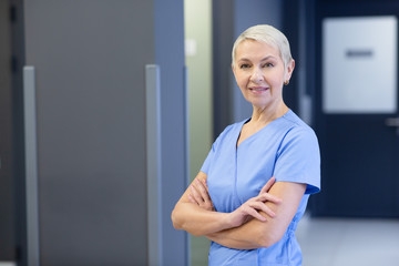 Portrait of a positively mature nurse at corridor of a modern clinic, looking at the camera....