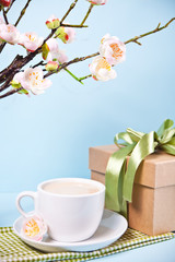 A cup of tea, gift box and cherry blooming with flowers sakura on the blue background. Spring concept. Copy space