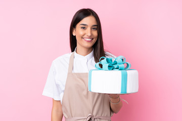 Young woman with a big cake over isolated background smiling a lot