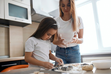 Cute little girl learning to knead the dough in the kitchen, mother teaching her, giving edvice. close up side view photo
