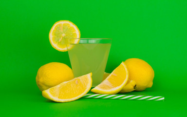  Glass with lemon juice and fresh lemons on a bright green background.