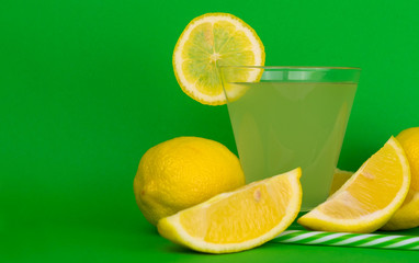  Glass with lemon juice and fresh lemons on a green background. Copy space.