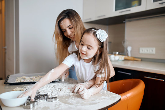 Mother Sprinkling Flour On The Dough For Cookies While Daughter Playing With Dough. Close Up Photo.kid Drawing Something On The Table With Finger In The Kitchen