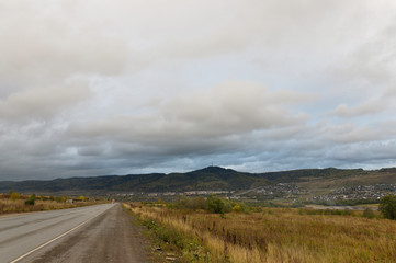Heavy grey clouds in the cold autumn sky over  village with small houses far away in the mountains and fields. Travelling. People living. Roads 