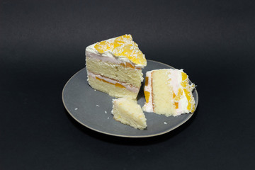 Pieces of holiday cake with white cream and juicy apricot on gray plate  on black background