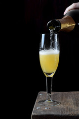 Champagne is being poured from the bottle into a champagne glass with citrus syrup. Process of making mimosa cocktail