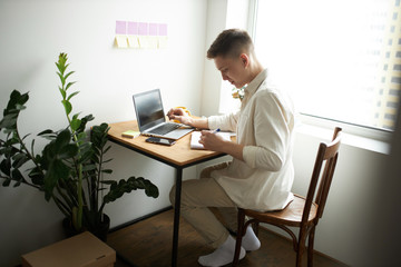 young journalist writing a report at home. close up side view photo. pleasant male designer writing on the notepad, notebook