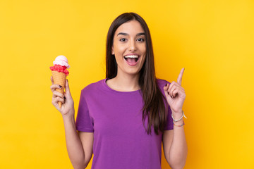 Young brunette woman with a cornet ice cream over isolated yellow background pointing up a great...