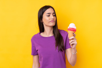Young brunette woman with a cornet ice cream over isolated yellow background with sad expression