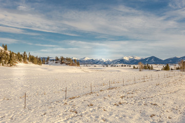 Large snowy field with vintage fencing and a vast mountain range in the distance on beautiful day