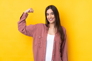 Young brunette woman over isolated yellow background doing strong gesture