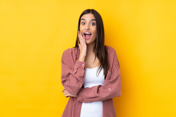 Young brunette woman over isolated yellow background surprised and shocked while looking right