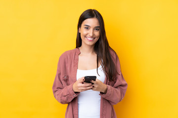 Young brunette woman over isolated yellow background sending a message with the mobile