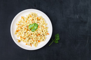 Vegetarian stewed side dish of brown rice with onions and carrots in a white plate on a black background. Traditional national cuisine