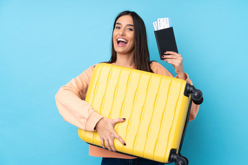 Young brunette woman over isolated blue background in vacation with suitcase and passport