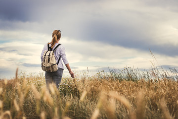 Woman with backpack hiking in field at summer