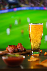 Spicy barbecue chicken wings, tomato salsa, nachos and beer on dark wooden bar table. Football on background, high resolution