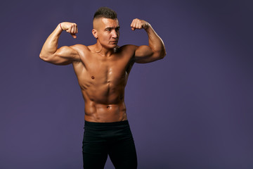 muscular shirtless sweaty bodybuilder raising his arms and showing biceps. Side view.close up...