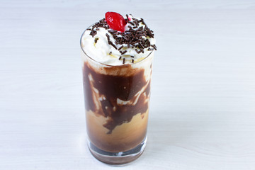 Glass of coffee and cream milkshake on white wooden background