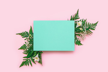 Creative layout made of flowers and leaves with paper card on pink background.