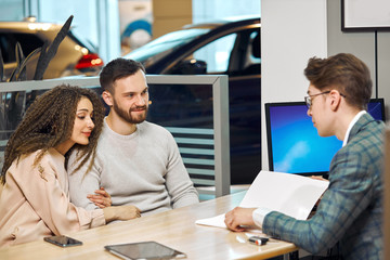 young couple choosing a car in the car canter, close up photo, young man in elegant grey suit having a business conversation with family