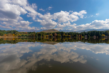 Obraz premium Clouds and autumn colored trees reflect on the water