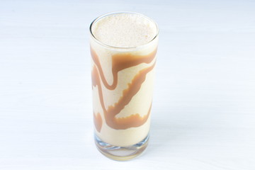Glass of coffee and cream milkshake on white wooden background