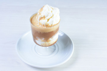 Cup of coffee with ice cream and coffee beans on white wooden background