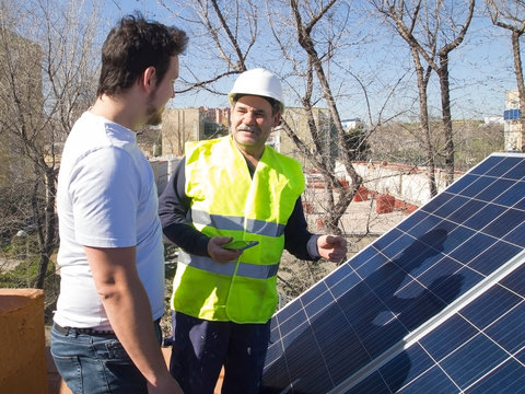 Caucasian seasoned technician talking to his young client beside the solar panels