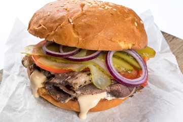 Tasty homemade burger consisting of bun, cheese, salad, red onion and tomato on an old wooden board