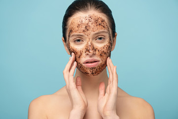 beautiful girl applying coffee scrub on face, isolated on blue