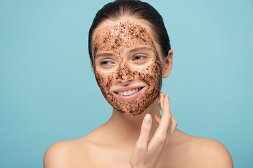 beautiful smiling woman applying coffee scrub on face, isolated on blue