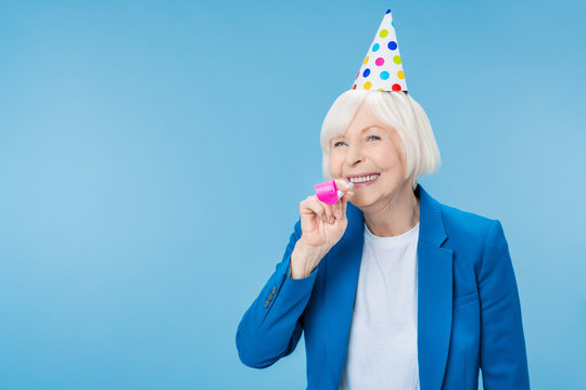 Happy Mature Woman In Party Hat Making Noise Isolated On Blue Background