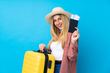 Young Uruguayan woman over isolated blue background in vacation with suitcase and passport