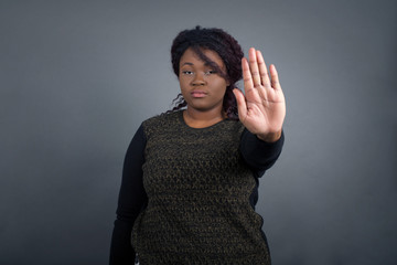 Young African American woman doing stop gesture with palm of the hand. Warning expression with negative and serious gesture on the face isolated over gray background.
