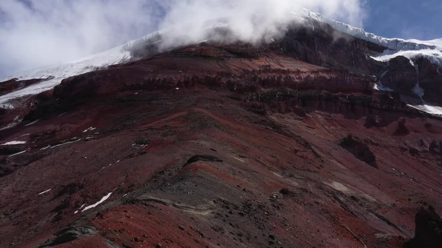 Aerial view that slowly flows over the edge of the mountain or vulcano chimborazo with red, black and grey sand and rocks