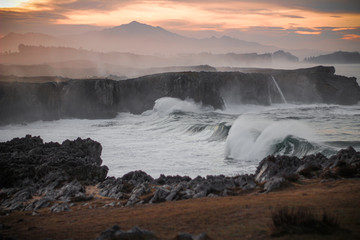 Ola rompiendo en un acantilado al atardecer 