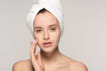 beautiful girl with towel on head applying coconut scrub on face, isolated on grey