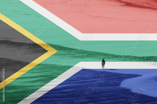 A South African flag with a women walking on a beach in the background. Tourism concept image.