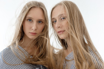 two young teenage pretty caucasian twin sisters in striped shirts with long matted blond hair looking at camera on white background.