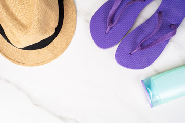 Close-up of a pair of flip-flops, hat and sunscreen.